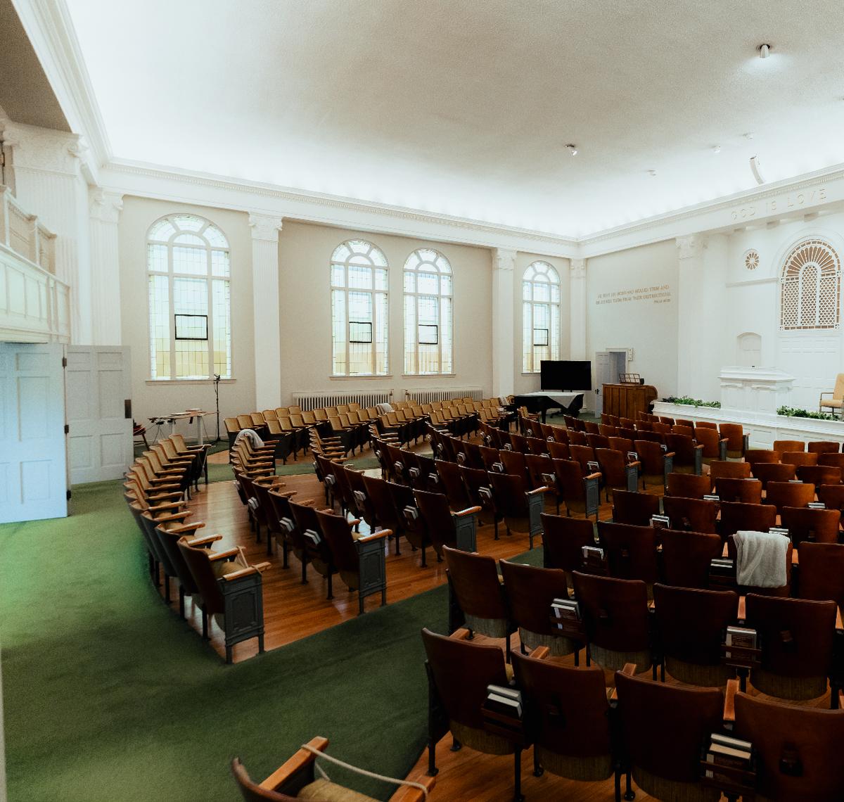 The sanctuary at 2243 13th Street: tall arched windows, a balcony, and curved rows of wooden theater seats